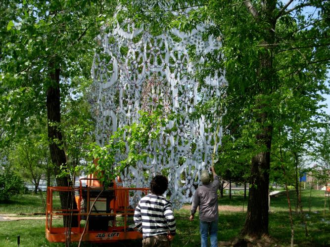 A large white doily is being installed between trees