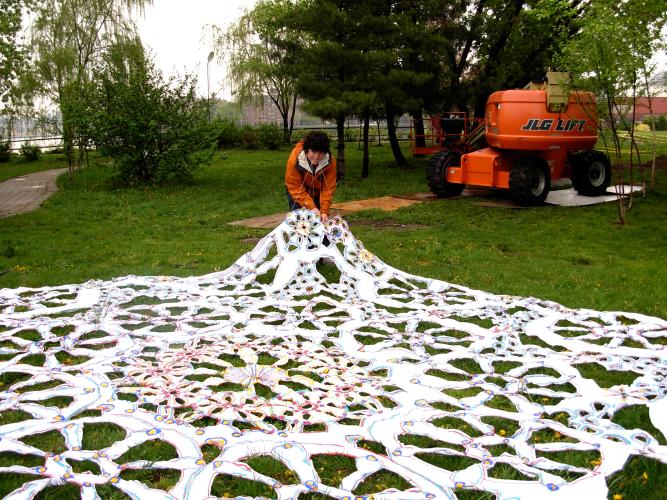Large white doily artwork lies on the ground outside