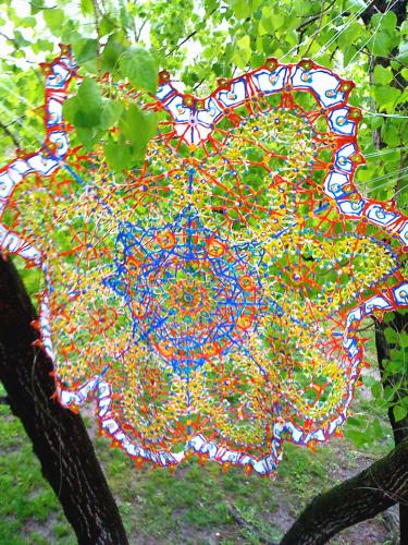 A primary-colored doily artwork hangs between two skinny trees