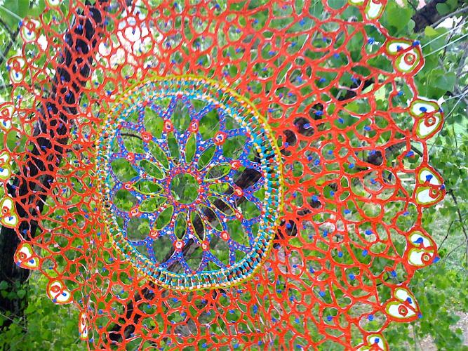 A large red and blue doily hangs among trees outside