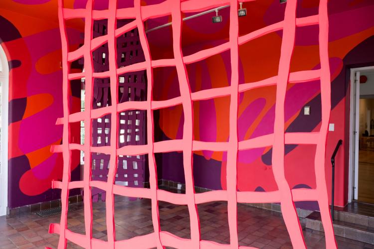 Close-up view of a fuchsia grid-like tapestry hanging in an art installation.