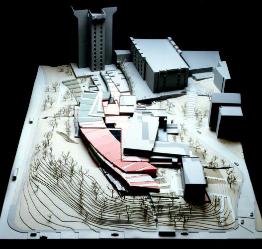 Model of a building complex surrounded by trees cascading down a gently sloping hill. 