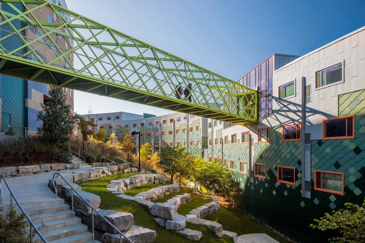 A skybridge provides a pathway to a building, crossing over a terraced slope. 