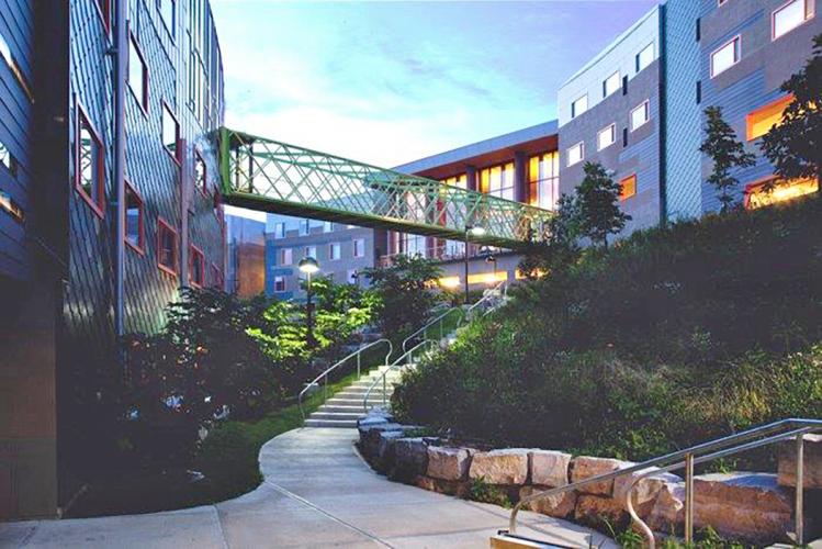 A skywalk bridge connects two buildings, crossing over stone stairs.