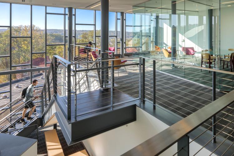 View of a staircase opening to a mezzanine balconied floor in front of a wall of windows.