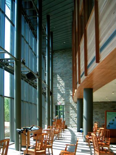 A mezzanine balcony overlooks an atrium lined with chairs in front of a windowed wall.