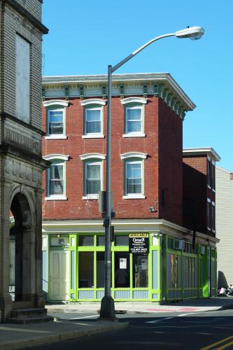 On a street corner sits a two-toned building with a bright lime green first story facade and a red brick facade on the top two stories.
