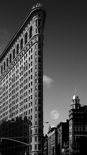 Black-and-white photo of NYC's Flatiron building and the moon in the distance.