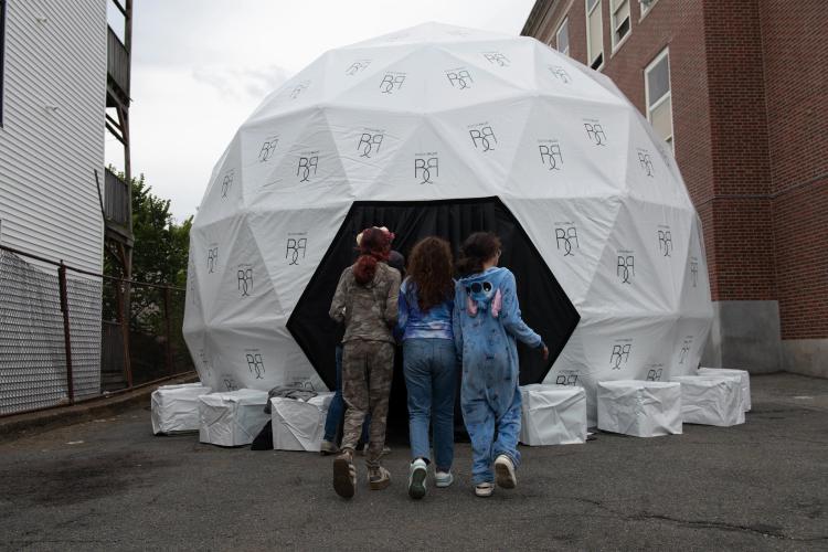 Three young women walk toward the entrance of a round white tent outside.