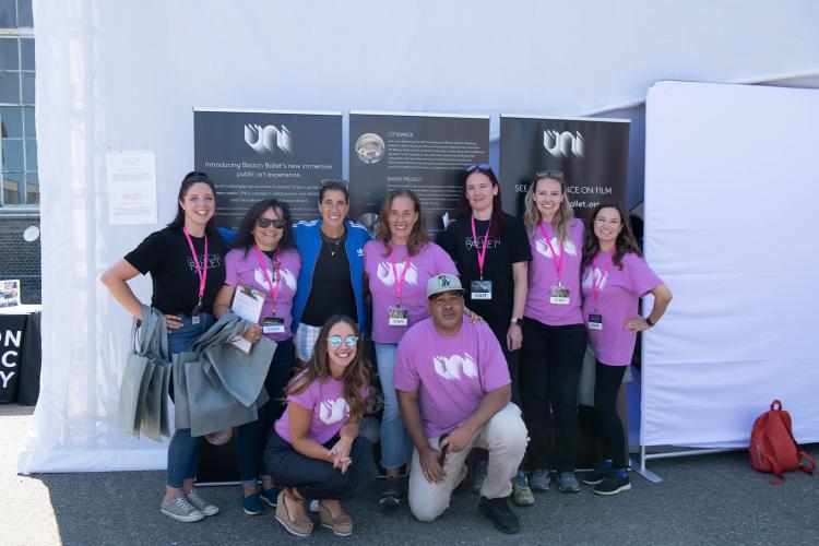 A group of adults dressed in shirts for Boston Ballet and Uni pose for a photo outside