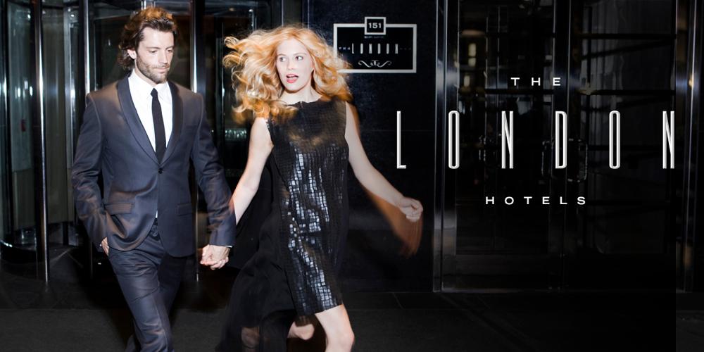 A blonde woman in a black dress holds hands with a man in a dark-colored suit as they exit The London Hotel