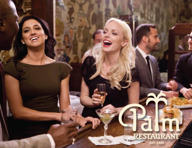 Two women are seated at a bar, laughing while enjoying drinks